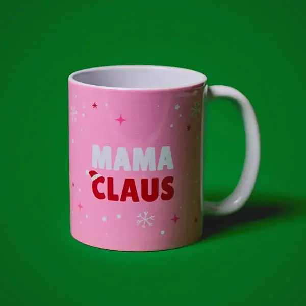 Pink Mama Claus Christmas mug with festive snowflake details displayed against a green background.